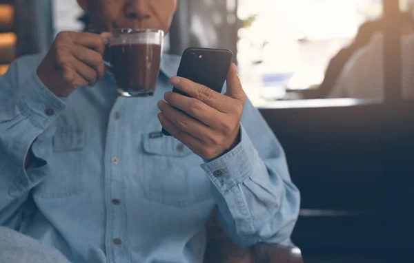 Casual business man drinking coffee and relaxed checking  application on smart phone, man using smartphone and browsing internet in cafe or coffee shop, internet network communication concept