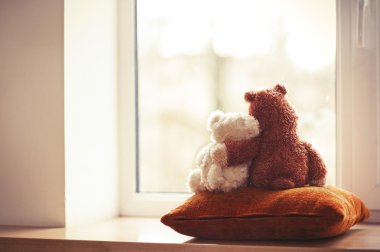 Two embracing teddy bear toys sitting on window-sill clipart
