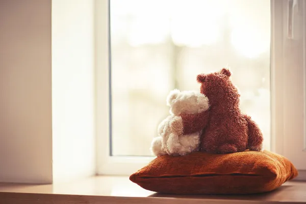 Two embracing teddy bear toys sitting on window-sill — Stock Photo, Image