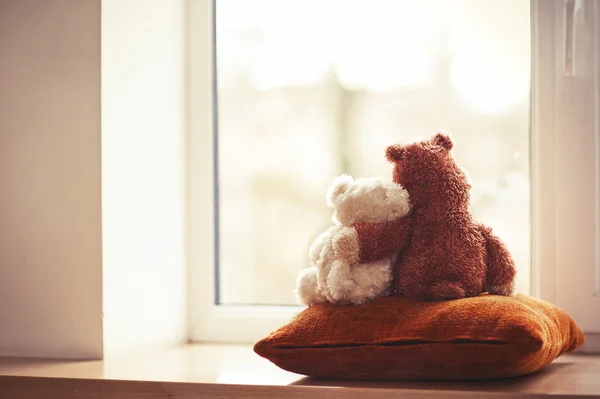 Two embracing teddy bear toys sitting on window-sill — Stock Photo, Image