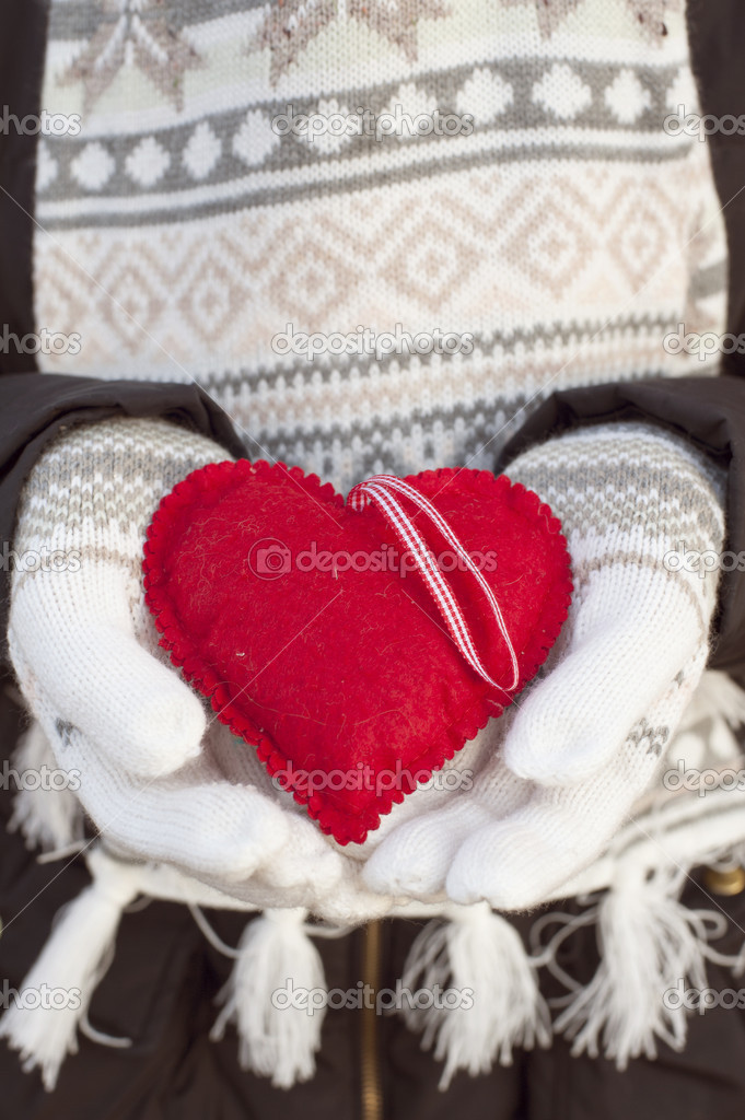 Female hands in white knitted mittens with romantic red heart