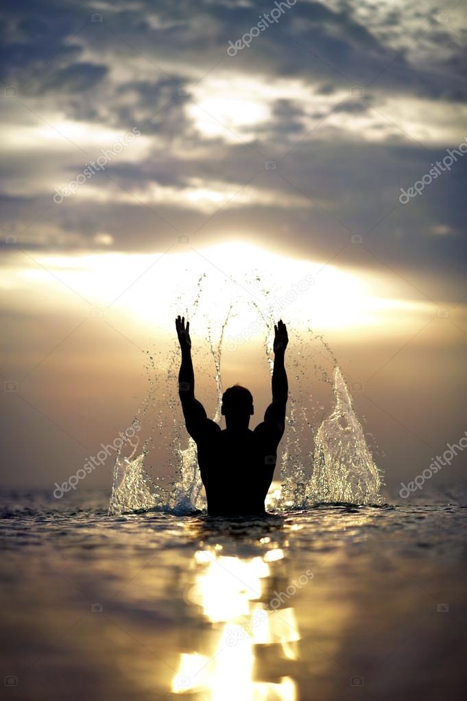 Man's silhouette with raised hands out of the sea with splash