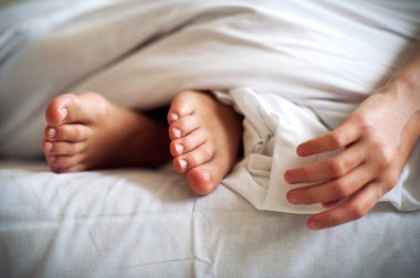 Sleeping child barefoot feet and hand on white bed linen. Indoor clipart
