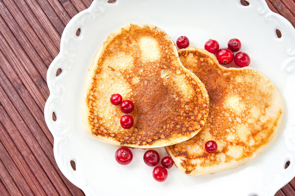 Heart shaped pancakes with cranberries on porcelain plate. Close
