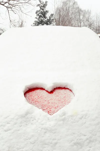 Love red heart shape in snow on red car. Close-up. — Stock Photo, Image