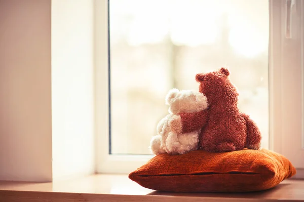 Two embracing loving teddy bear toys sitting on window-sill — Stock Photo, Image