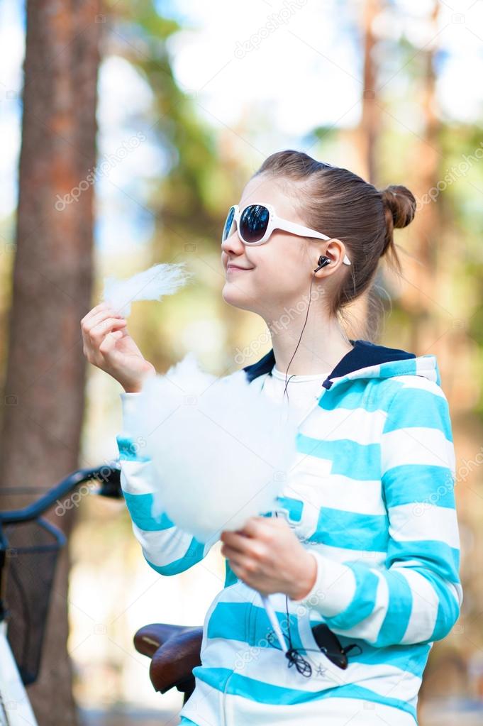 Smiling girl with cotton candy in summer park. Treat and happiness
