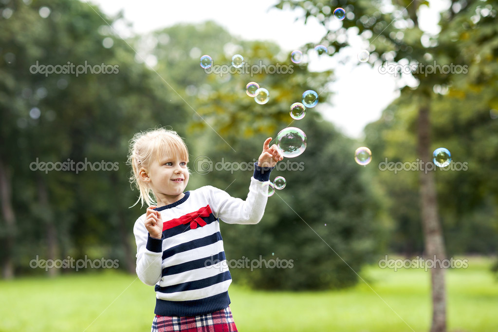 Little blonde playing girl with soap bubbles in green summer par