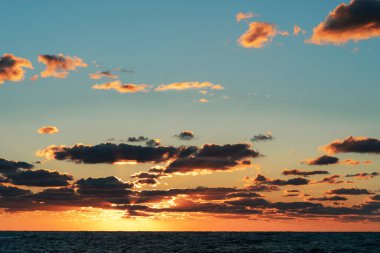 Deniz ve gökyüzünde bulutlarla güzel, parlak gün batımı