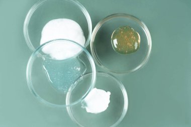 Kozmetik ürünler, fırça, yüz serumu ve yeşil arka planda birçok petri kabında jel. Bitkisel malzemelerin doğal kozmetikleri. Kozmetikte bitkiler ve temel yağlar.