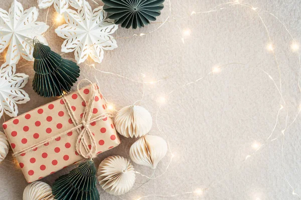 Bej renkli bir halıdaki bej kağıt hediye kutuları Noel süslerini ve kağıttan yapılmış Noel süslerini aydınlatıyor. Yeni yıl kutlaması konsepti.