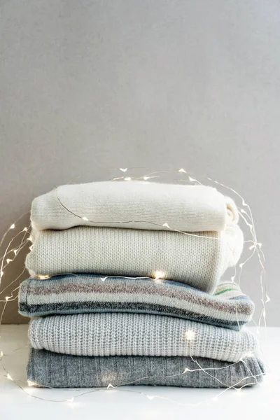 Pila de suéteres de lana de punto en diferentes colores decorados con luces de guirnalda de Año Nuevo. — Foto de Stock