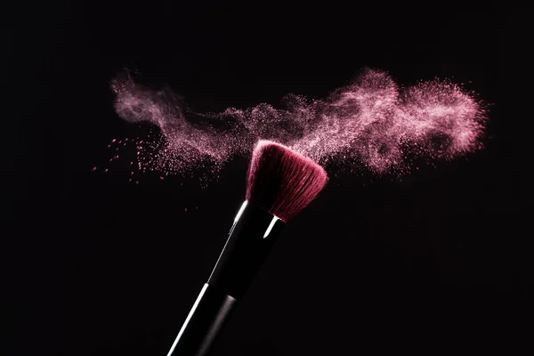 Pembe tozlu makyaj fırçası siyah arka planda patlama yapıyor. Güzellik konsepti. Kozmetik arkaplan.