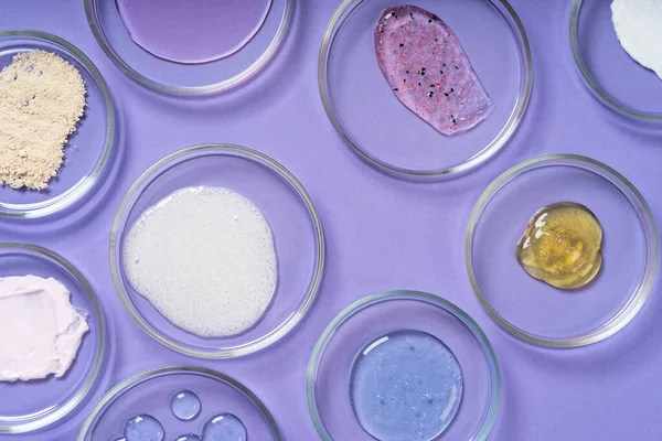Cosmetic products, scrub, face serum and gel in many petri dishes on a pink background. Cosmetics laboratory research concept. Pastel violet background
