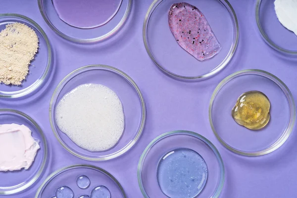 Cosmetic products, scrub, face serum and gel in many petri dishes on a pink background. Cosmetics laboratory research concept. Pastel violet background Fotografias De Stock Royalty-Free