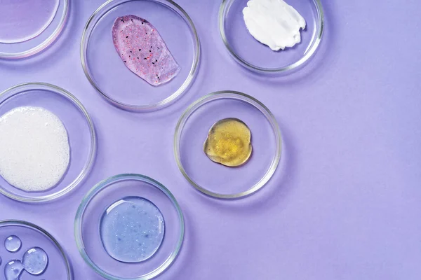 Cosmetic products, scrub, face serum and gel in many petri dishes on a pink background. Cosmetics laboratory research concept. Pastel violet background Imagem De Stock