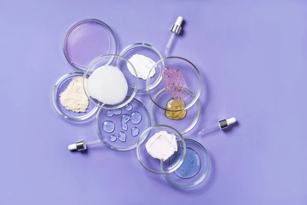 Cosmetic products, scrub, face serum and gel in many petri dishes on a pink background. Cosmetics laboratory research concept. Pastel violet background Imagens Royalty-Free