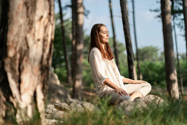 Uzun esmer saçlı güzel bir kadın güzel bir ormanda meditasyon yapıyor. Seyahat ve sağlıklı yaşam tarzı, doğanın keyfi.