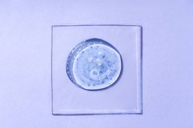 Kozmetik ürün damlaları veya menekşe arkaplanda kabarcıklar olan sıvı şeffaf jel.