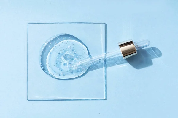 Gotas de produto cosmético ou gel transparente líquido com bolhas em um fundo azul. Imagem De Stock