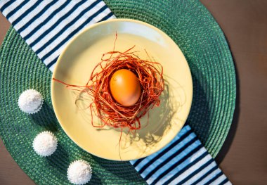 Turuncu renkli çimen yuvasına yerleştirilmiş organik yumurta yeşil masa örtüsü üzerinde siyah beyaz çizgili tekstil peçetesiyle yeşil tabakta. Boşluğu kopyala