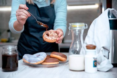 Sarışın kadın reçelli ve sütlü çörek yiyor, mutfakta oturuyor, rahat yemeğin tadını çıkarıyor. Seçici odak