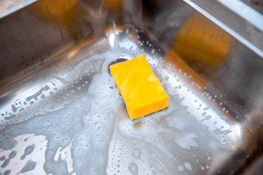 Mutfak lavabosundaki sarı sünger yakın plan. Evdeki kirleri ve mikropları temizlemek.