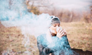 Kadın doğada şöminenin yanında çay ya da kahve içer.
