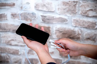 Çoklu kablo cep telefonu şarjı. Erkek el, şarj etmek için elektrik gücüne bağlanan akıllı telefonu tutuyor. Boşluğu kopyala