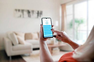 Ev otomasyonu için akıllı telefon uygulaması kullanan bir kadın. Sarışın kadın akıllı evi mobil bir cihazdan kontrol ediyor.