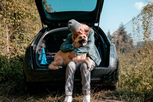 Arabasının bagajında köpeğiyle oturan bir kadın gezgin. Yol arasında dinleniyorum.