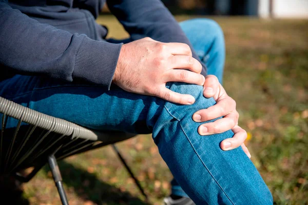 Erkek elleri dışarıda dizlerini tutuyor. Menüsküs ağrısı çeken bir erkek.