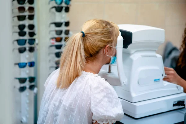 Doctor ophthalmologist examining eyesight of patient with special medical device. Blonde Caucasian Female at Comprehensive eye exams by a doctor of optometry