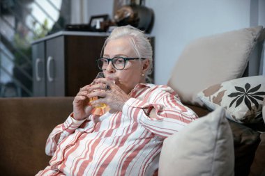 Kafkas kıdemli bayan dinlenirken bir bardak taze suyla kanepede oturuyor. Yaşlı beyaz saçlı büyükanne suyla ferahlatıyor.