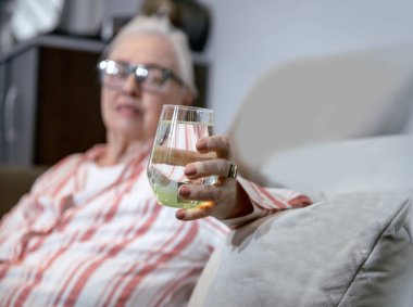 Kafkas kıdemli bayan dinlenirken bir bardak taze suyla kanepede oturuyor. Yaşlı beyaz saçlı büyükanne suyla ferahlatıyor.