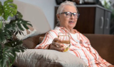 Kafkas kıdemli bayan dinlenirken bir bardak taze suyla kanepede oturuyor. Yaşlı beyaz saçlı büyükanne suyla ferahlatıyor.