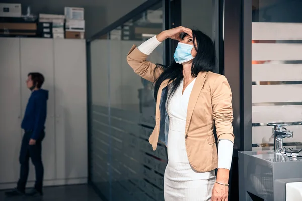 Worried Business Woman with face mask in front of office, having headache and problems at work