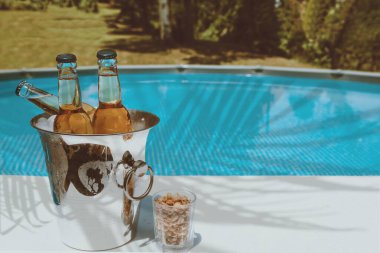 Bira şişeli buz kovası ve havuz kenarında fıstık. Tropik tatil rahatlaması. Boşluğu kopyala