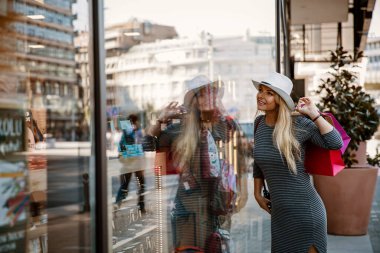 Şehirde alışveriş yapan, vitrinlere bakan bir kadın. Güzel, sarışın, uzun saçlı, alışveriş torbaları olan bir kadın.