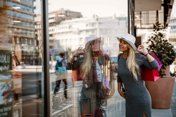 Şehirde alışveriş yapan, vitrinlere bakan bir kadın. Güzel, sarışın, uzun saçlı, alışveriş torbaları olan bir kadın.