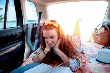 Bagajdaki genç kadın, arabada battaniyeye uzanıyor.