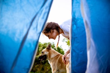 Genç ve mutlu bir kadın çoban köpeğiyle kamp yaparken çadırda eğleniyor.