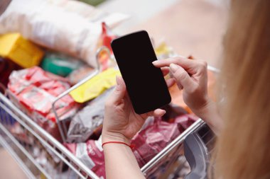 Akıllı telefonda yazan bir kadın tam müşteri alışveriş arabasına yaslanıyor. Marketteki yiyecek listesini kontrol ediyorum. Kadın ellerinde boş siyah telefon ekranı