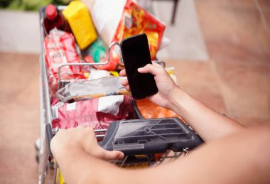 Akıllı telefonda yazan bir kadın tam müşteri alışveriş arabasına yaslanıyor. Marketteki yiyecek listesini kontrol ediyorum. Kadın ellerinde boş siyah telefon ekranı