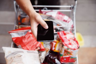 Akıllı telefonda yazan bir kadın tam müşteri alışveriş arabasına yaslanıyor. Marketteki yiyecek listesini kontrol ediyorum. Kadın ellerinde boş siyah telefon ekranı