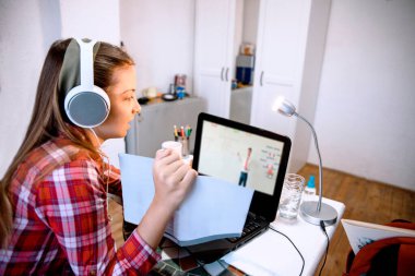 Genç Kız online eğitim başvurusu için dizüstü bilgisayar kullanıyor. Coronavirus salgını sırasında evdeki video sınıfındaki çocuk