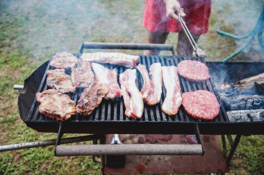 Kız açık havada barbekü ızgarasında hamburger hazırlıyor. Genç kadın elleri açık ızgarada taze et yapıyor.