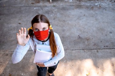 Kırmızı Kumaş Giyen Genç Kız okula giderken elinde kitaplarla yüz maskesi dikmiş. Yeniden kullanılabilir maske takan uzun saçlı bir bayan öğrenci. Boşluğu kopyala