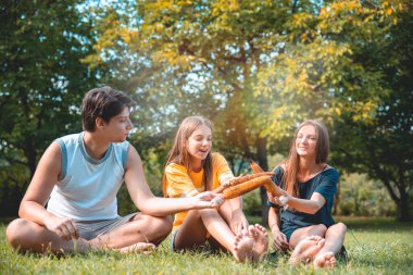 Güneşli bir günde çimlerin üzerinde oturmuş mısır yiyen gençler. Gençler piknikte kızarmış mısırın tadını çıkarırlar. Doğadaki arkadaşlar mısır yer. 