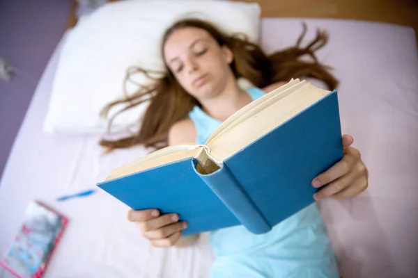 Teenage cute Girl smiling with book in hands while laying on bed. Reading a Book for school work. Above view